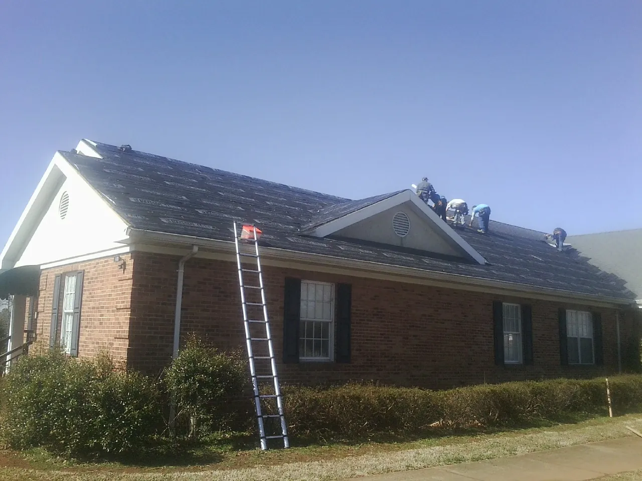 Crew tearing shingles off a brick ranch roof with a ladder set — Emergency Roof Repair work by our crew in Racine
